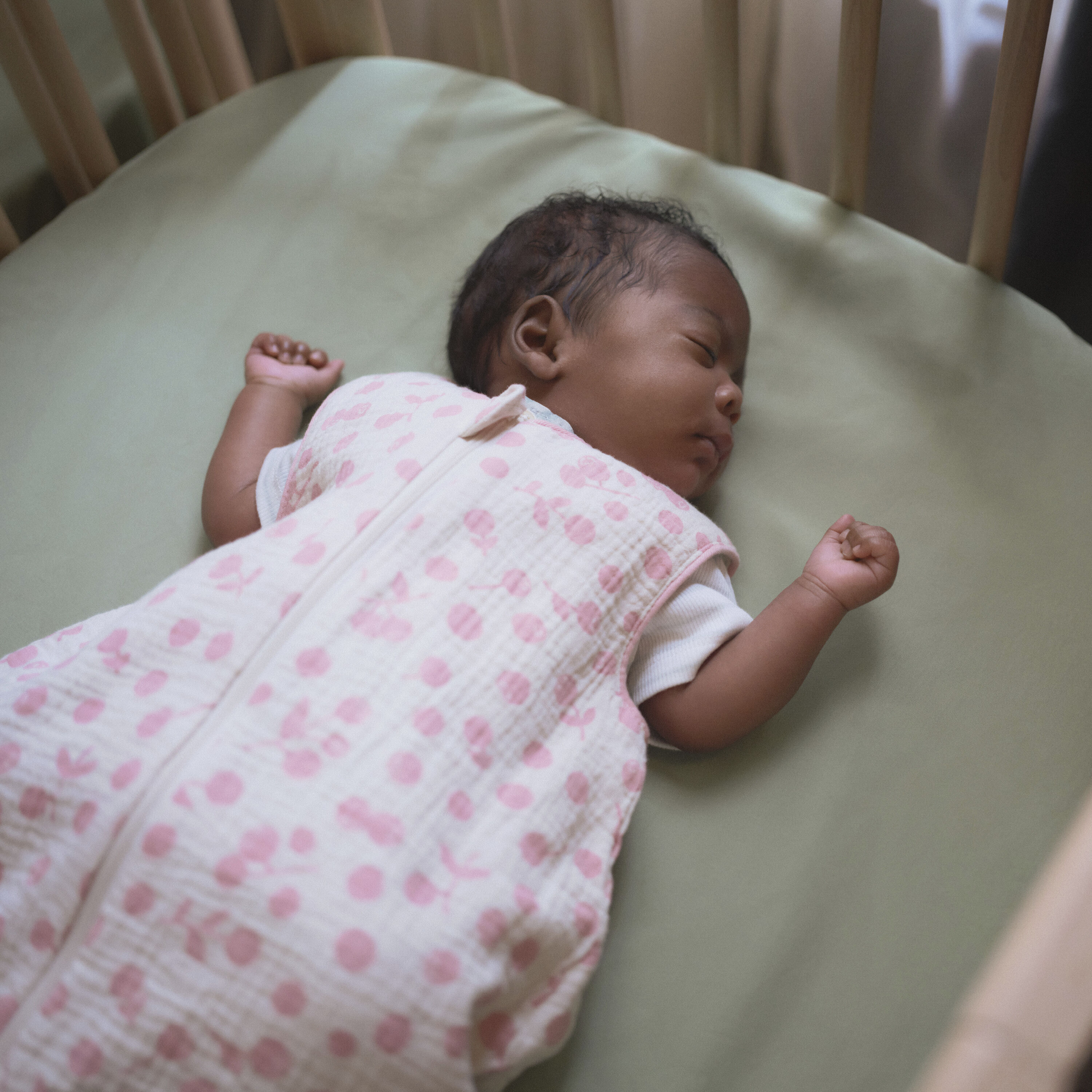 A parent gently settling a newborn into a Stokke® Nighti™ cot in a calm, softly lit Scandinavian nursery — illustrating secure, purposeful nursery furniture designed for everyday newborn care.