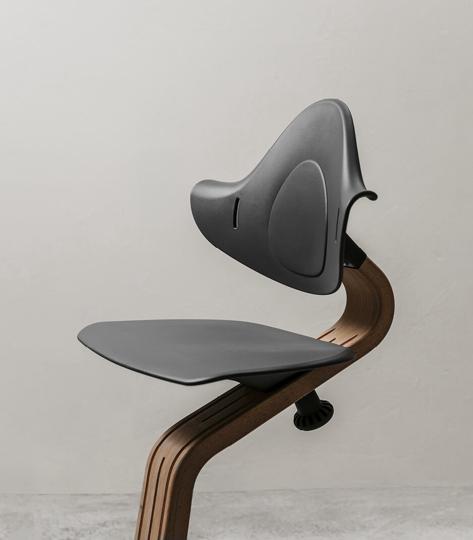 Stokke® Nomi® Chair. Walnut premium wood and Anthracite plastic parts. Styled/detail.