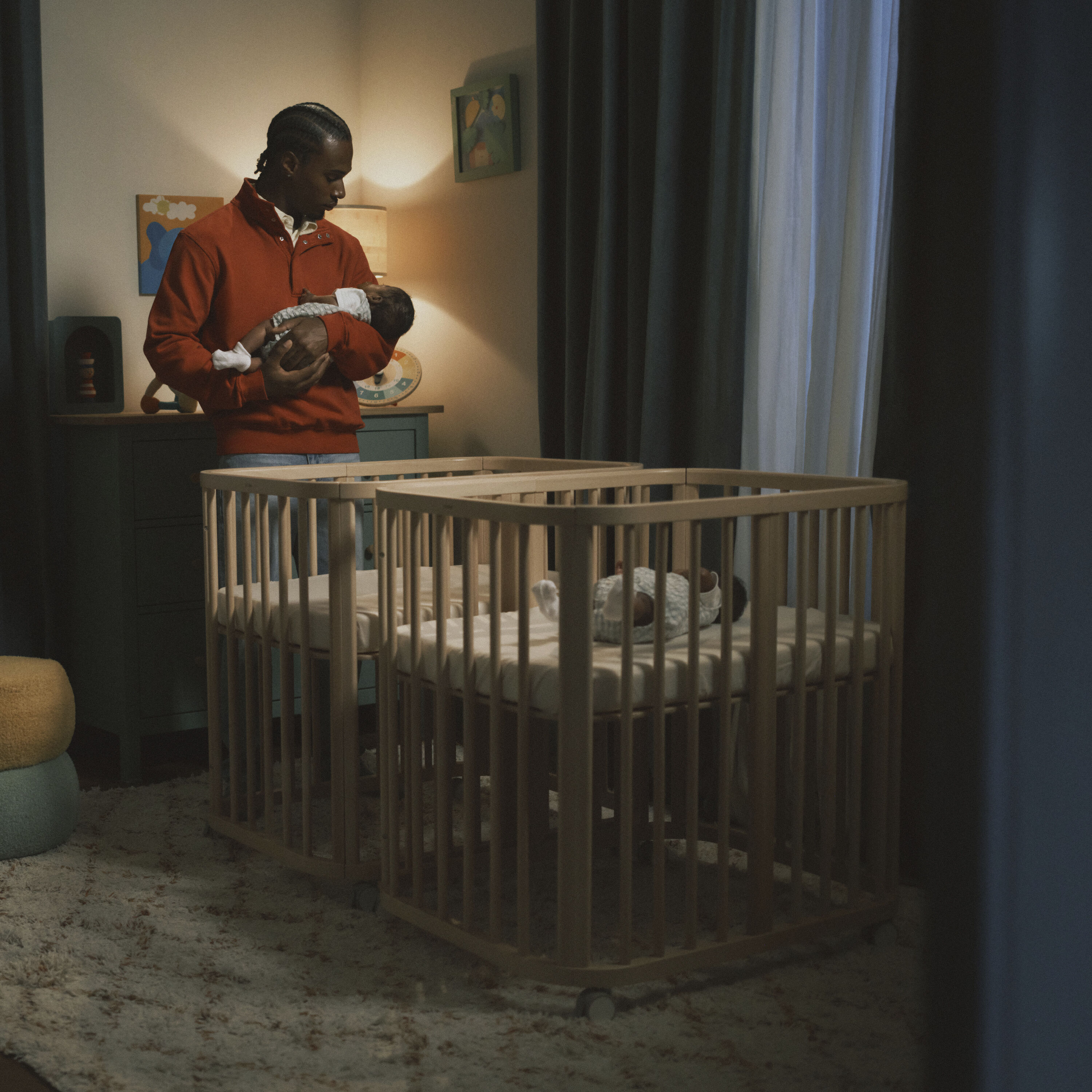 A peaceful baby sleeps in a Stokke Sleepi™ oval wooden crib in a softly lit nursery with natural wood furniture and neutral tones.