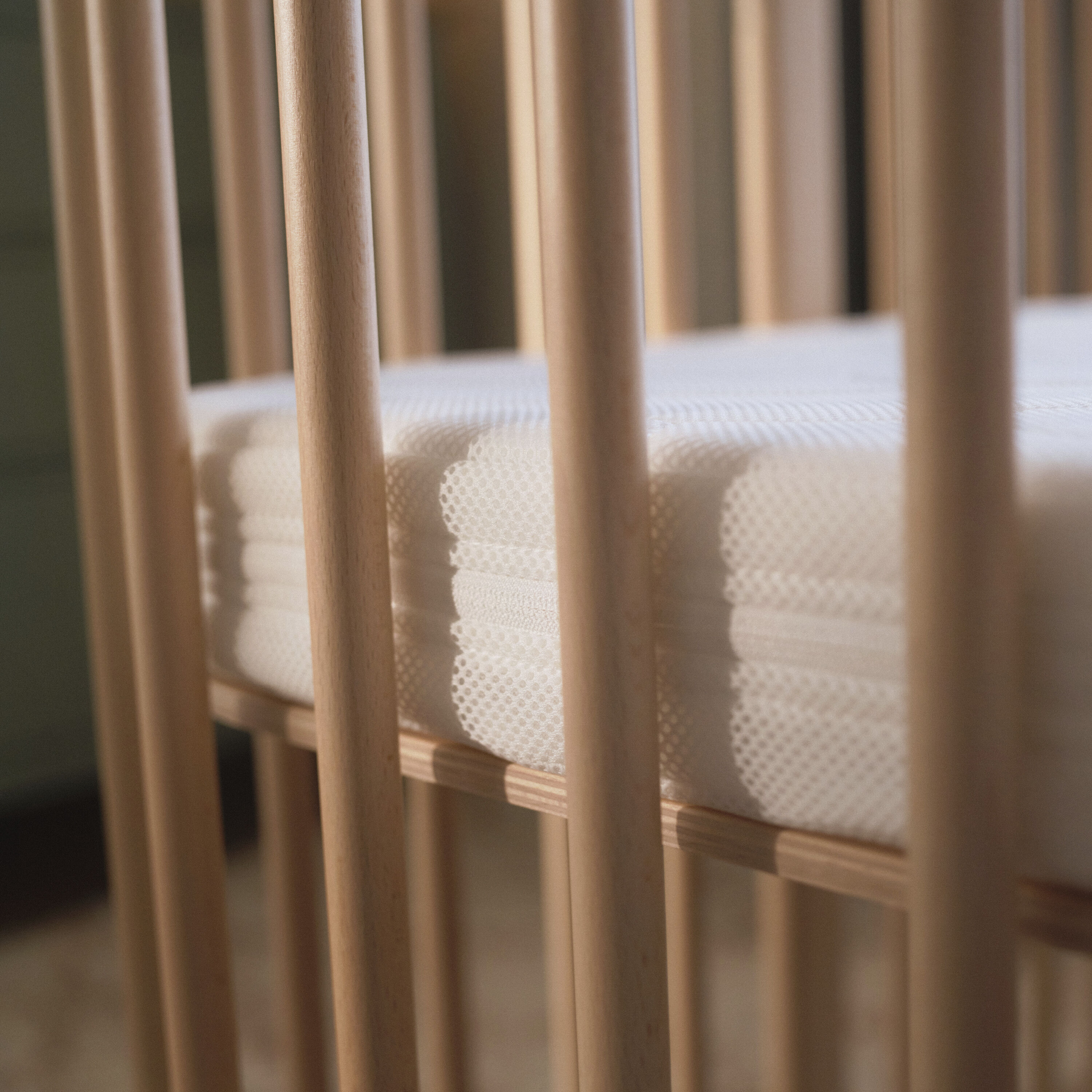 Stokke® Nighti™ cot bed in a warm, softly lit nursery — a lifestyle image showing the natural beechwood cot in a calm Scandinavian home setting.