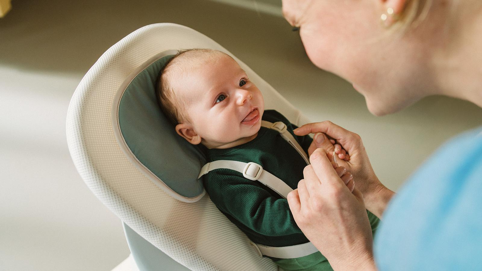 Un bambino nel Newborn Set di un seggiolone Tripp Trapp tiene il dito di un adulto, guardando giocosamente in alto.