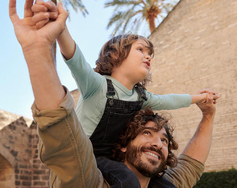 Child on father's shoulders pretending to fly.