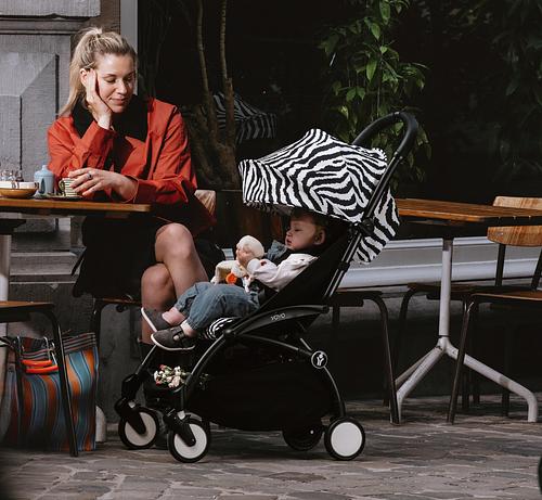 Moeder zit op een terras naast een YOYO-kinderwagen met dierenprint.
