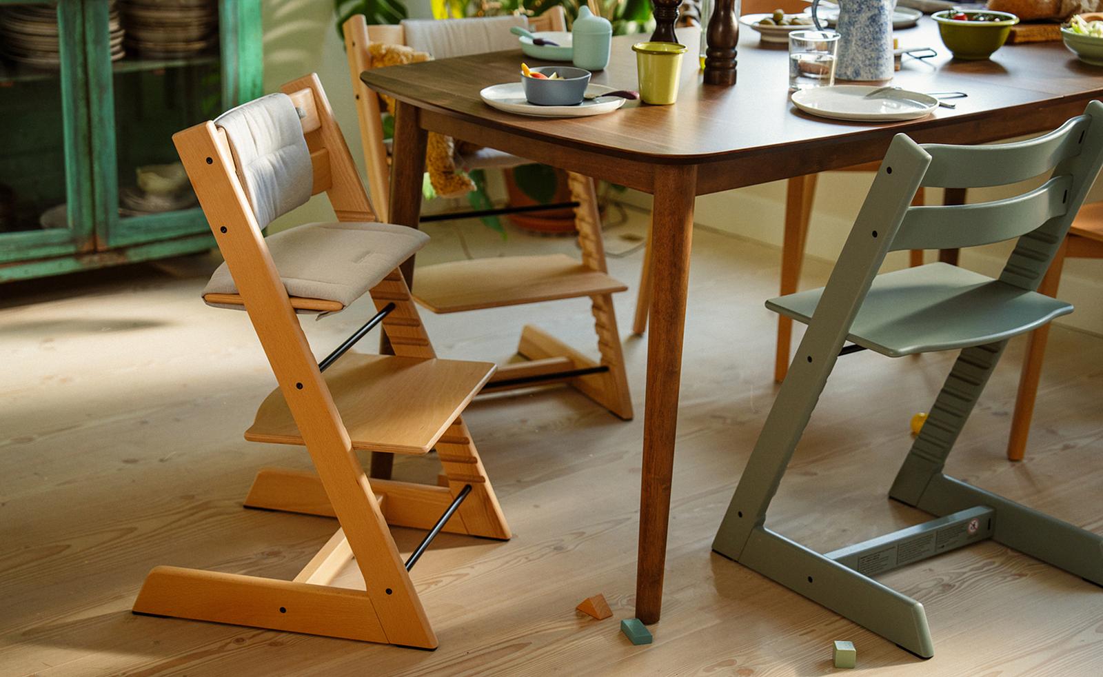 Two Tripp Trapp chairs, natural wood with cushion and green, at a dining table set for a meal.
