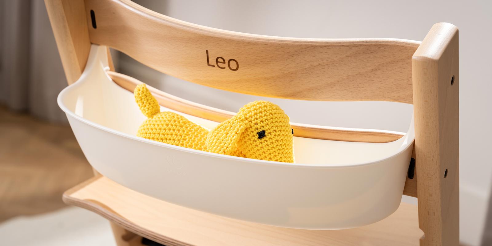 Tripp Trapp barnstol med ett vitt Newborn Set, personifierad med 'Leo', som håller en gul ankleksak.