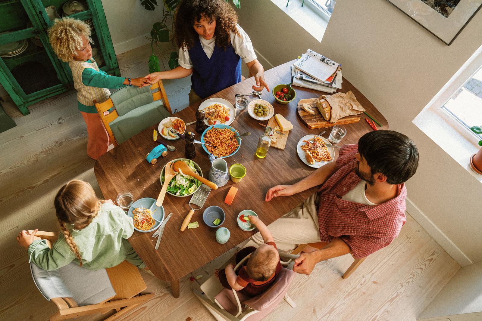 Famiglia di cinque persone che mangia spaghetti. Bambini seduti su una sedia Tripp Trapp e un seggiolone STOKKE YOYO.