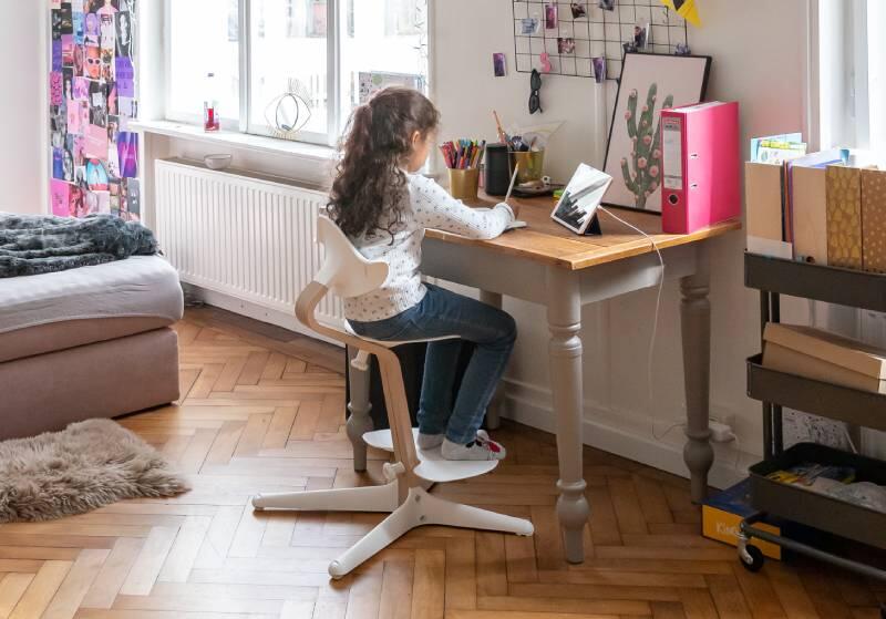 Image of a young girl sitting in her room at her desk writing in her journal in her Stokke® Nomi® chair.