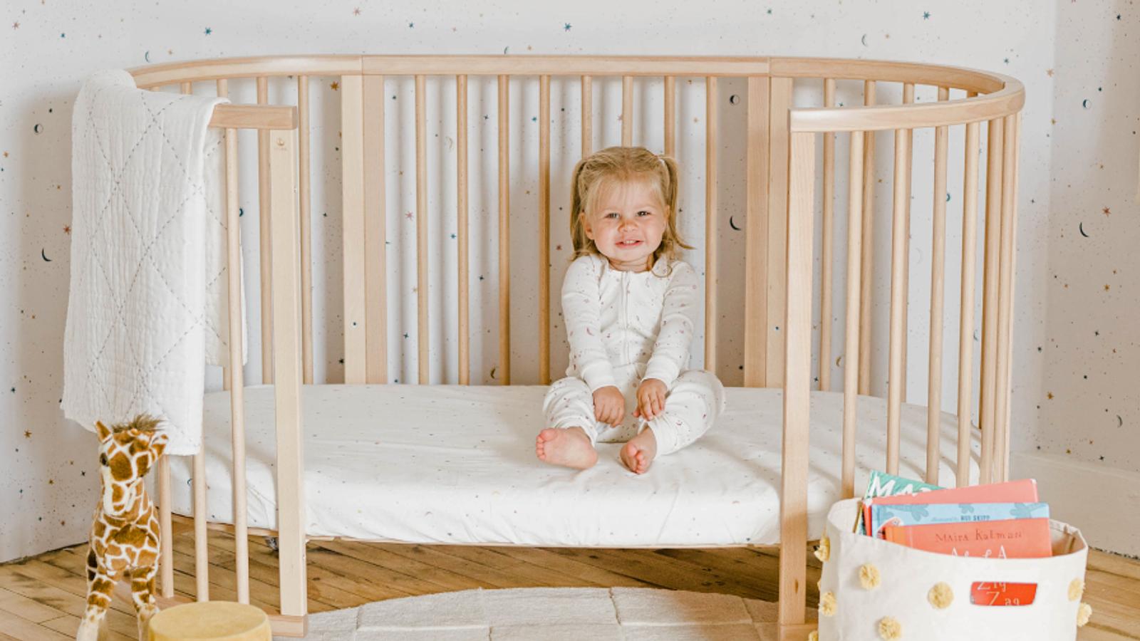 Girl in Stokke Sleepi Bed Crib with Pehr sheets in her nursery.