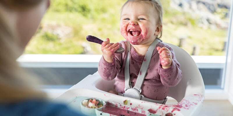 Baby in a white Clikk high chair getting messy while eating a berry smoothie from its ezpz tray.