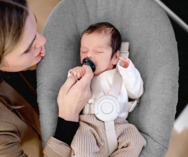 Mother looking down at baby resting in the Stokke® Nomi® chair with newborn set.