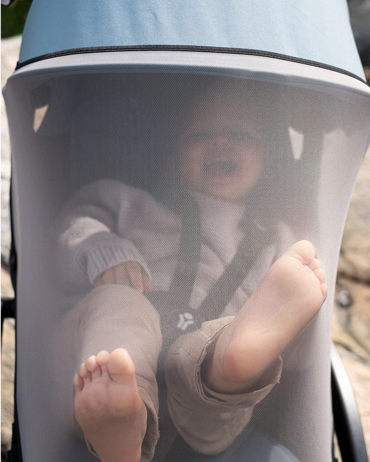 Bébé dans une poussette STOKKE YOYO couverte d'une moustiquaire, montrant ses pieds nus.
