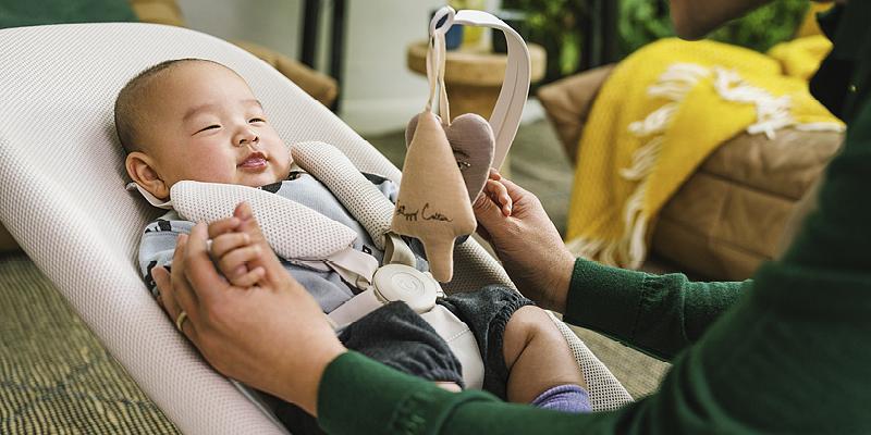 Baby is playing with a toy, while laying in YOGA Baby Bouncer