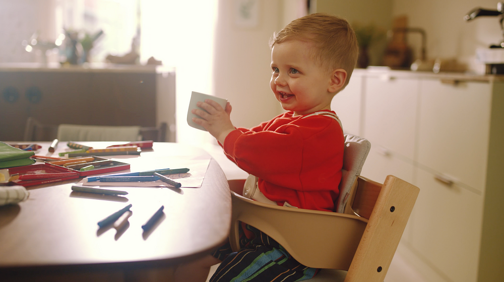 Toddler in red shirt sits in beige Tripp Trapp®