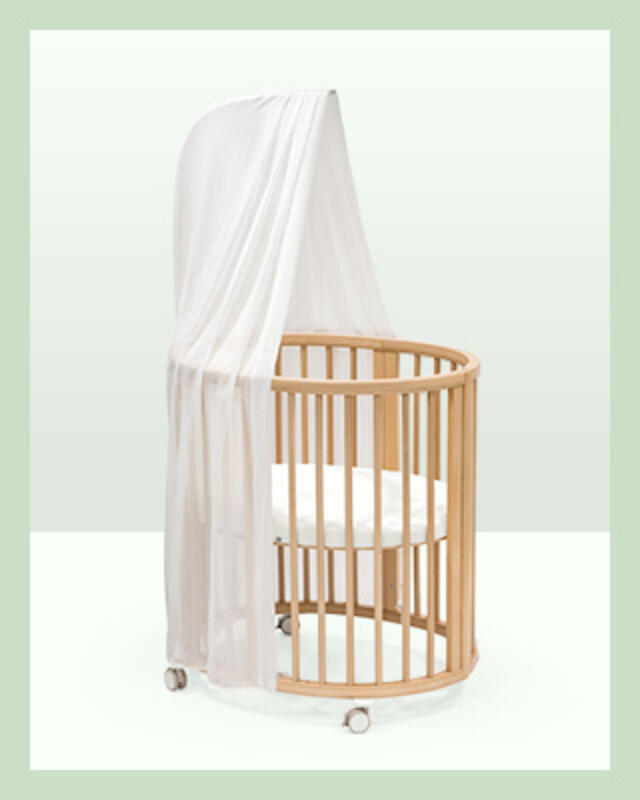 A Sleepi mini crib in natural wood color with white mattress and canopy.