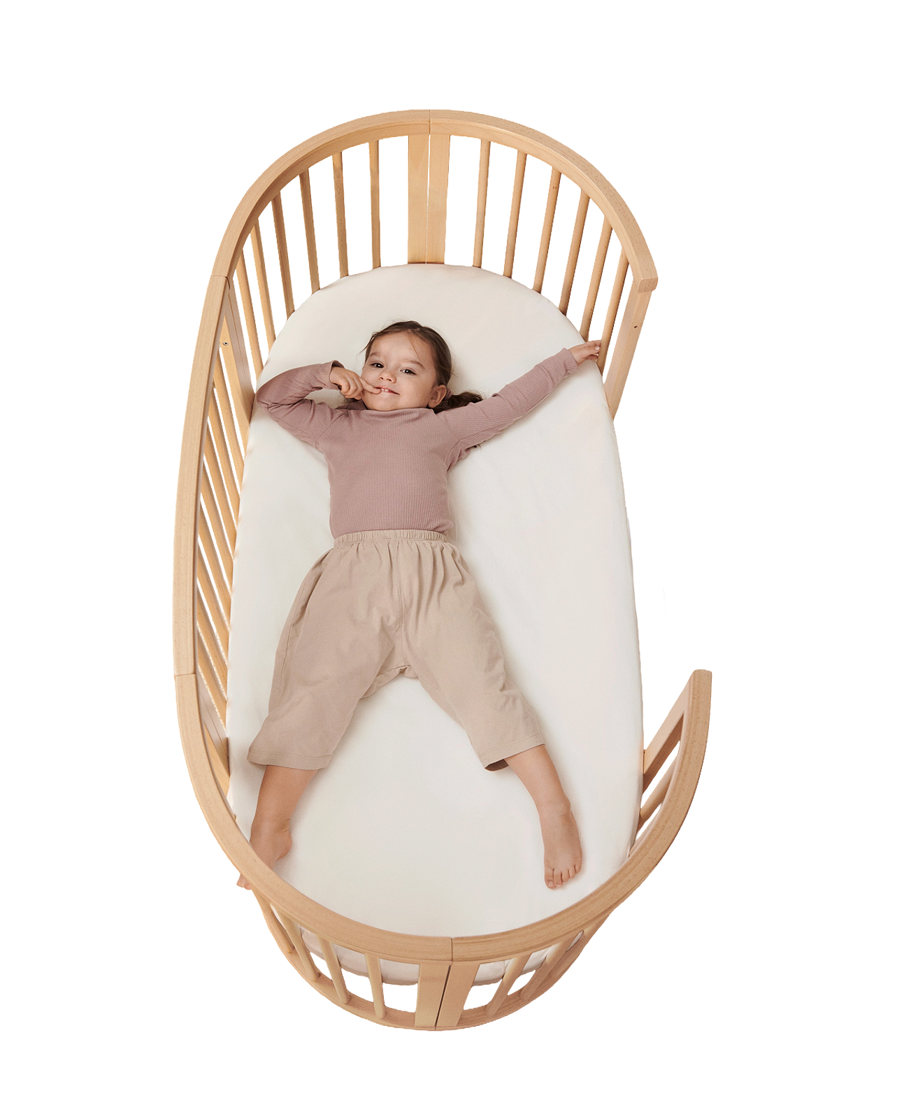 笑顔の子供が木製のSTOKKE Sleepiベビーベッドに仰向けに横たわっています。