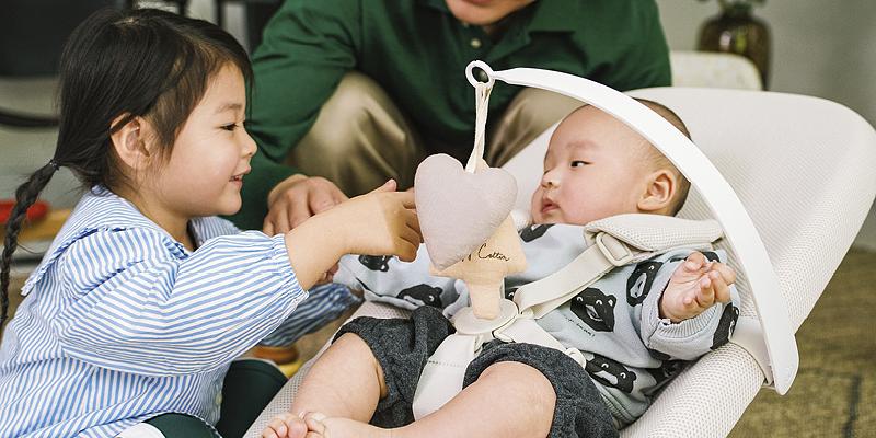Infant is playing with their sibling while laying in Yoga bouncer