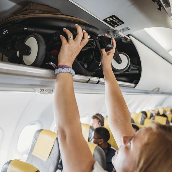 Femme rangeant une poussette Stokke YOYO pliée dans le compartiment à bagages d’un avion.