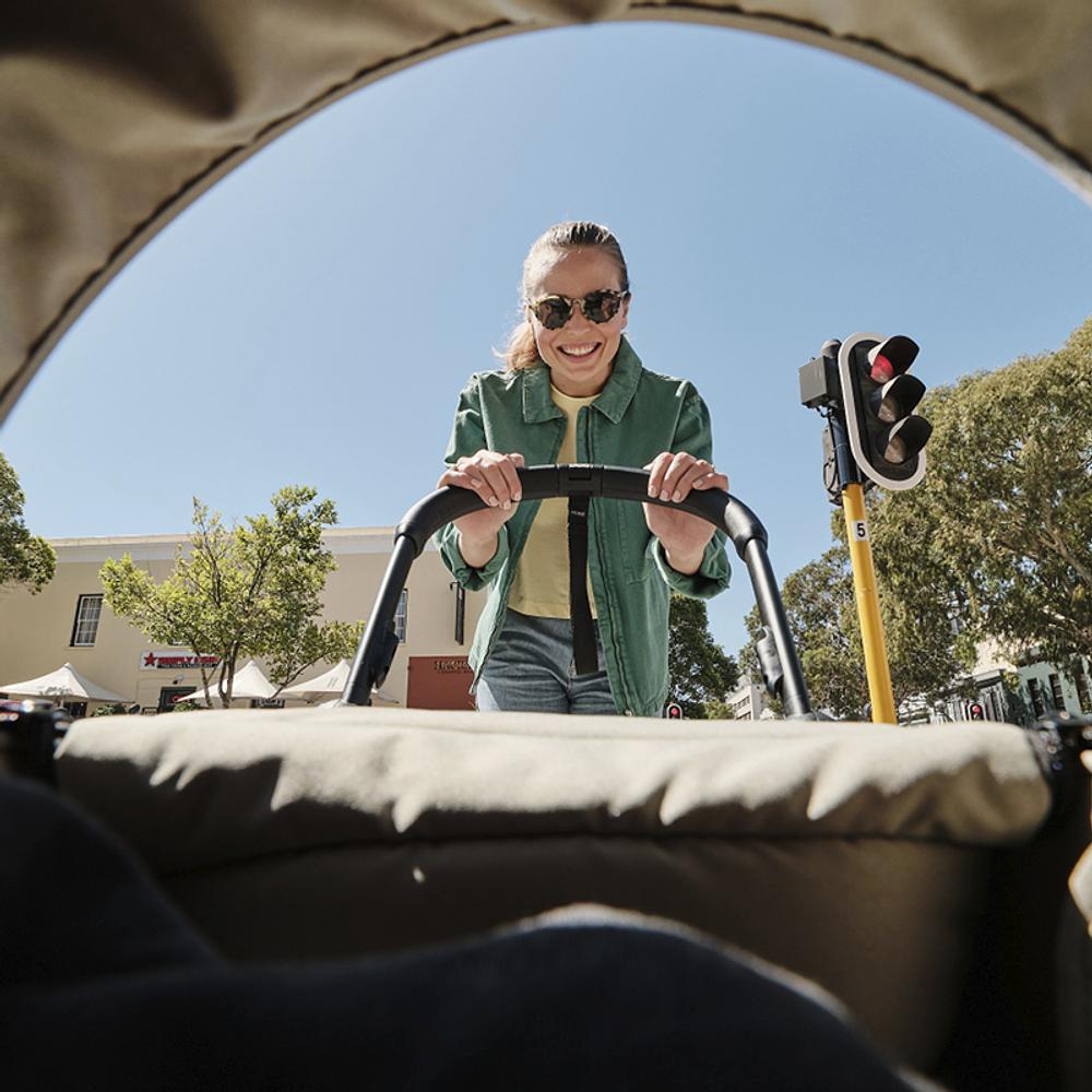 Mujer sonriente empujando un cochecito de viaje Stokke YOYO en un día soleado.