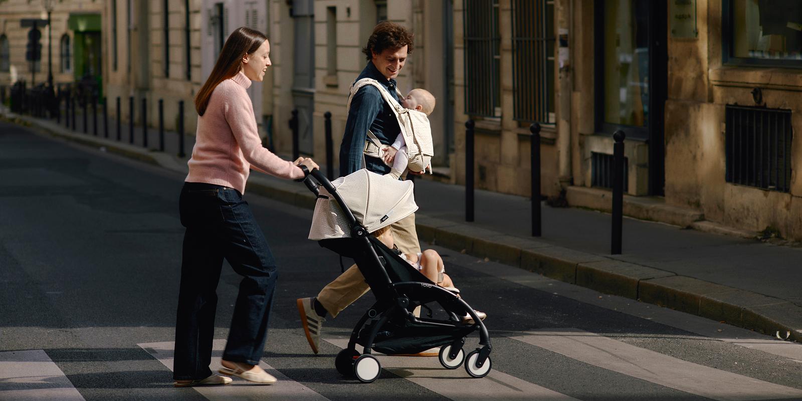 Couple walks a city street. Woman pushes a STOKKE YOYO stroller, man carries a baby.
