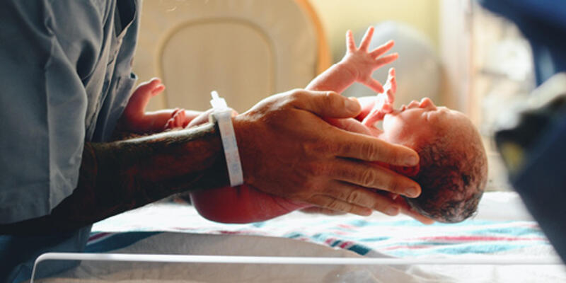 Man in the hospital placing a newborn baby in a hospital bassinet to rest.