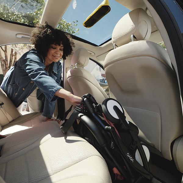 Femme plaçant une poussette de voyage Stokke YOYO pliée sur la banquette arrière d’une voiture.