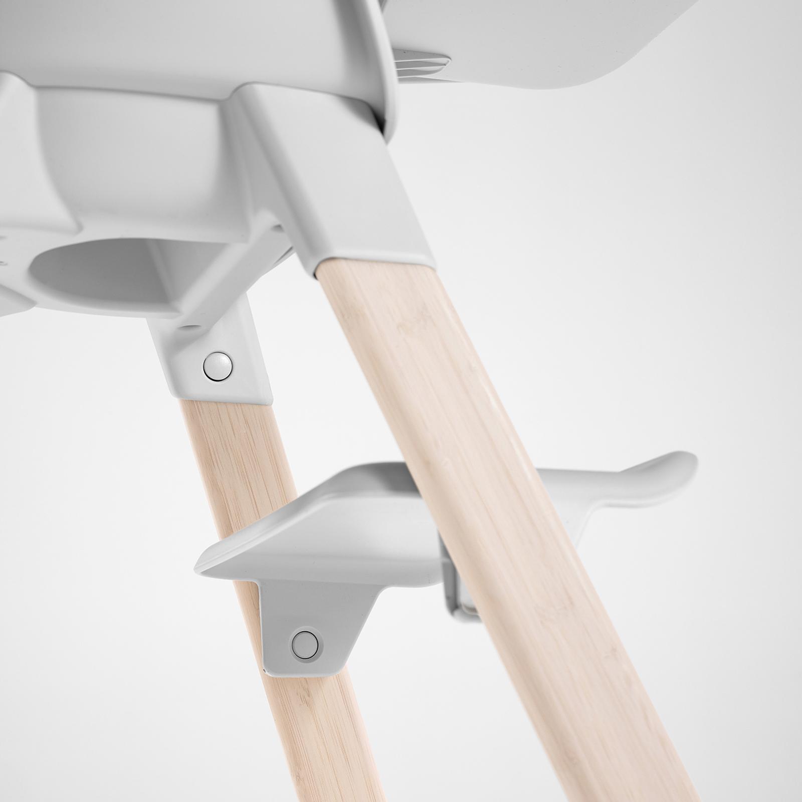 Primo piano di un seggiolone Tripp Trapp con gambe in legno naturale e componenti bianchi.