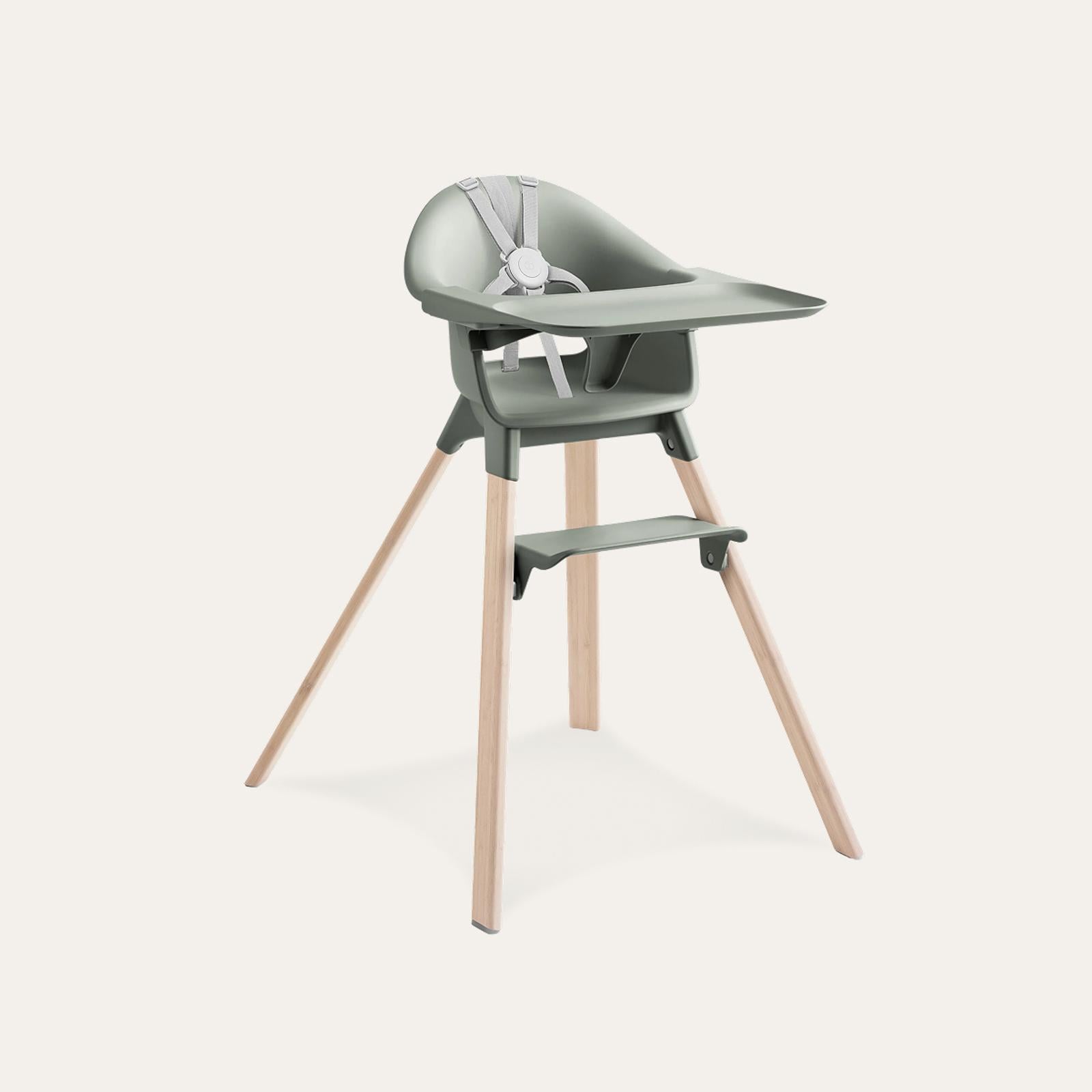 A modern high chair with sage green seat, tray, and footrest, on light wooden legs with a grey harness.