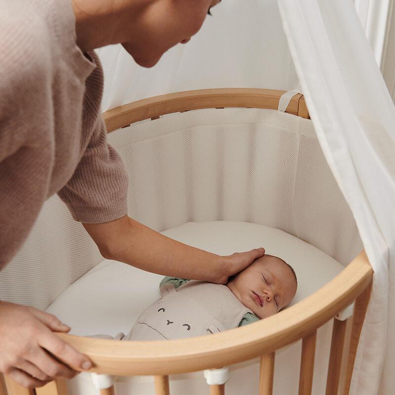 Mom putting newborn baby into sleepi mini crib.