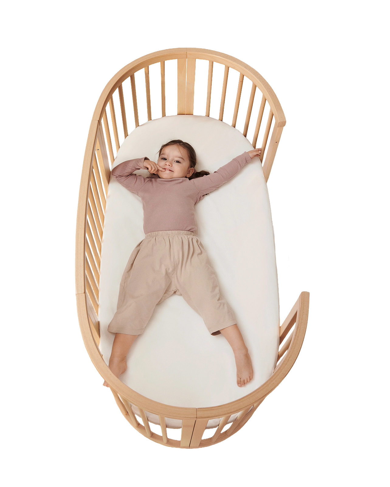 A smiling child lies outstretched in a wooden STOKKE Sleepi crib.