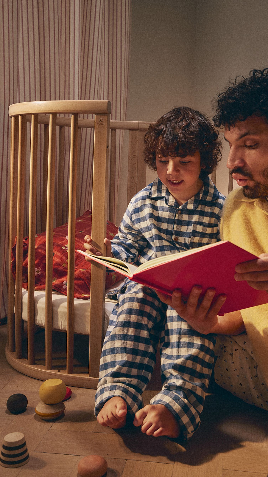 Father and child read a bedtime story by a Stokke Sleepi crib.