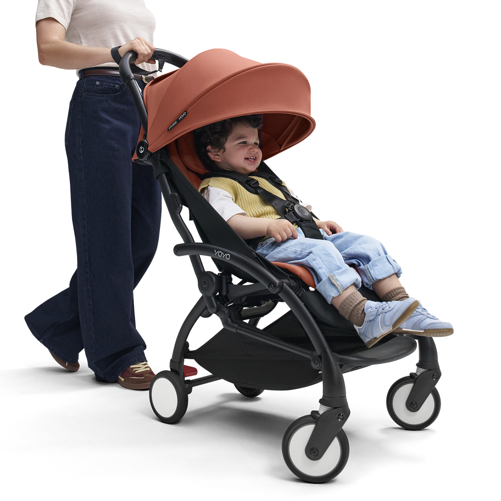 A woman pushes a happy child in a terracotta STOKKE YOYO stroller.
