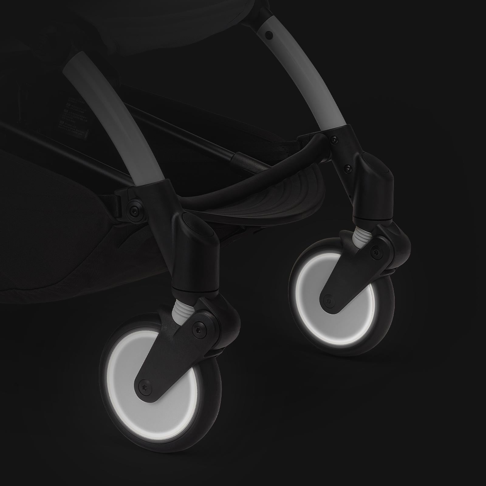 Primer plano de las ruedas delanteras de un cochecito STOKKE YOYO, que brillan sobre un fondo oscuro.