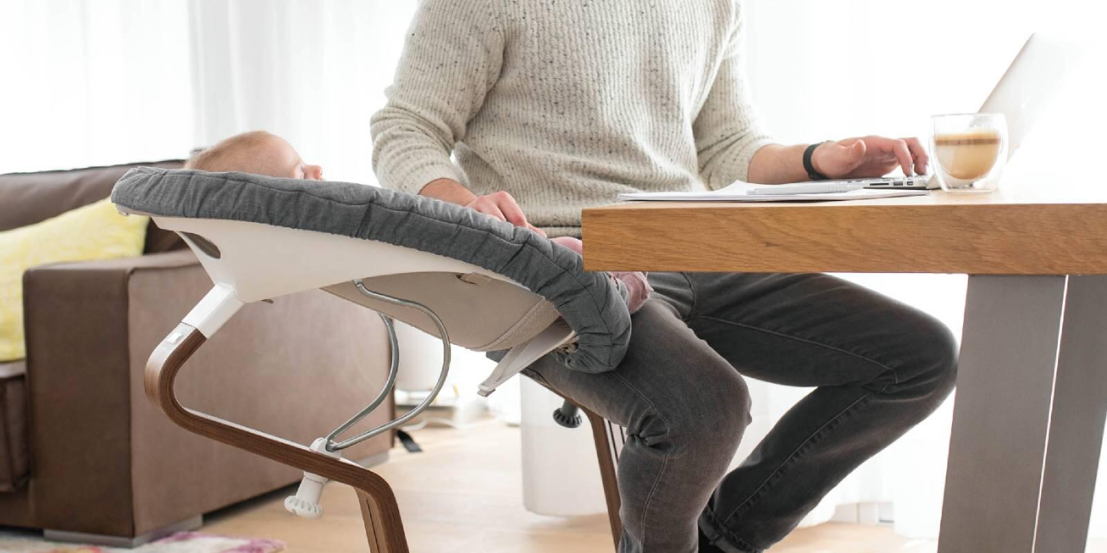 Image of a newborn baby in the Stokke® Nomi® chair with newborn set next to Dad.
