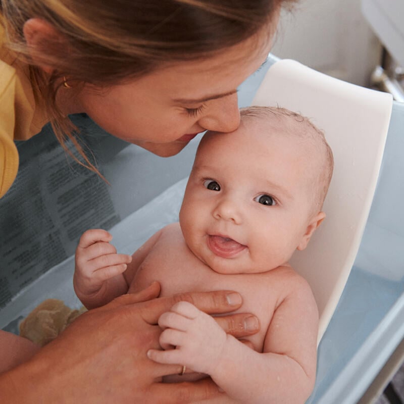 Мать купает новорожденного ребенка, используя гибкую ванночку с подставкой для новорожденного.