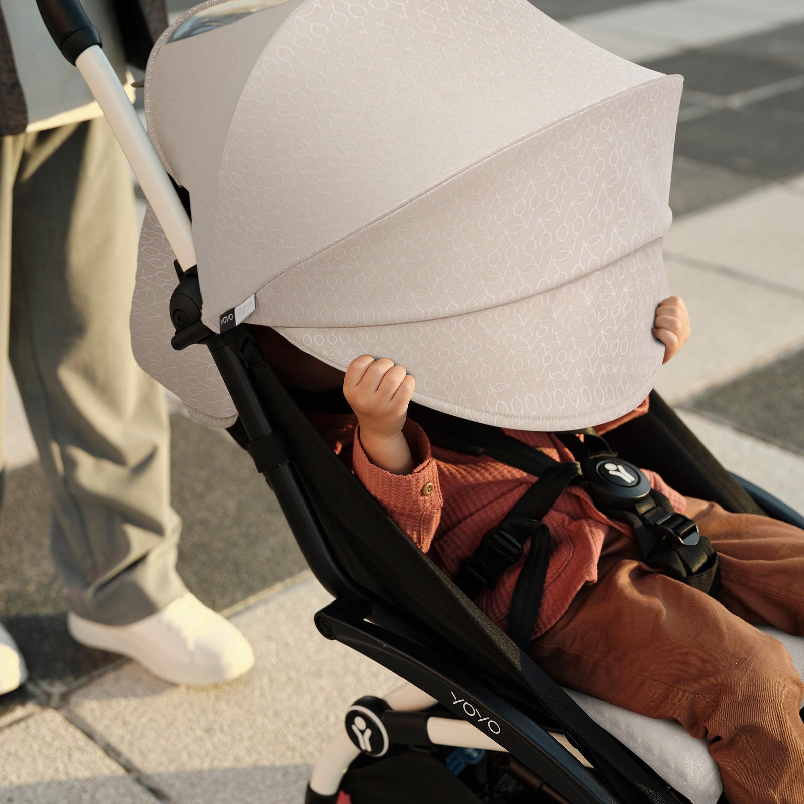 柄入りのベージュのキャノピーが付いたSTOKKE YOYOベビーカーに乗った赤ちゃんが、遊びながらキャノピーを引き下げています。