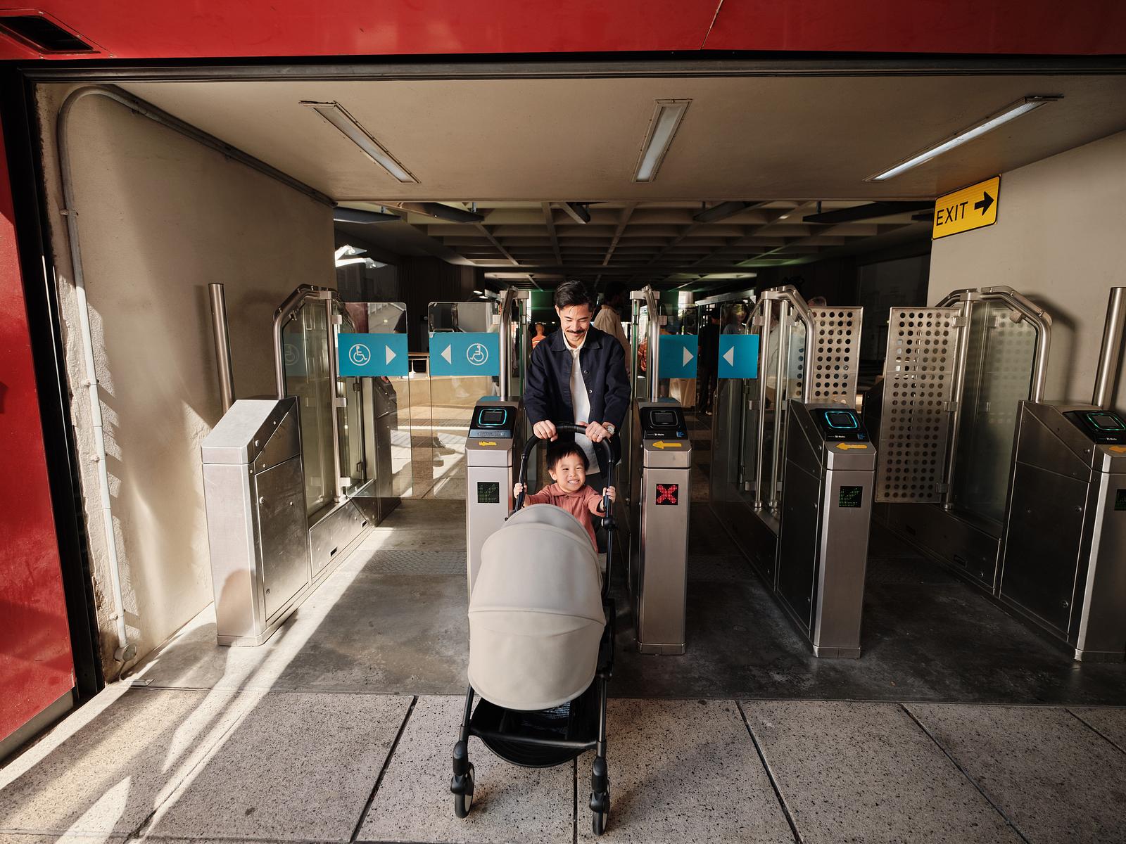 Un homme pousse un enfant souriant dans une poussette STOKKE YOYO à travers les portiques de la station de métro.
