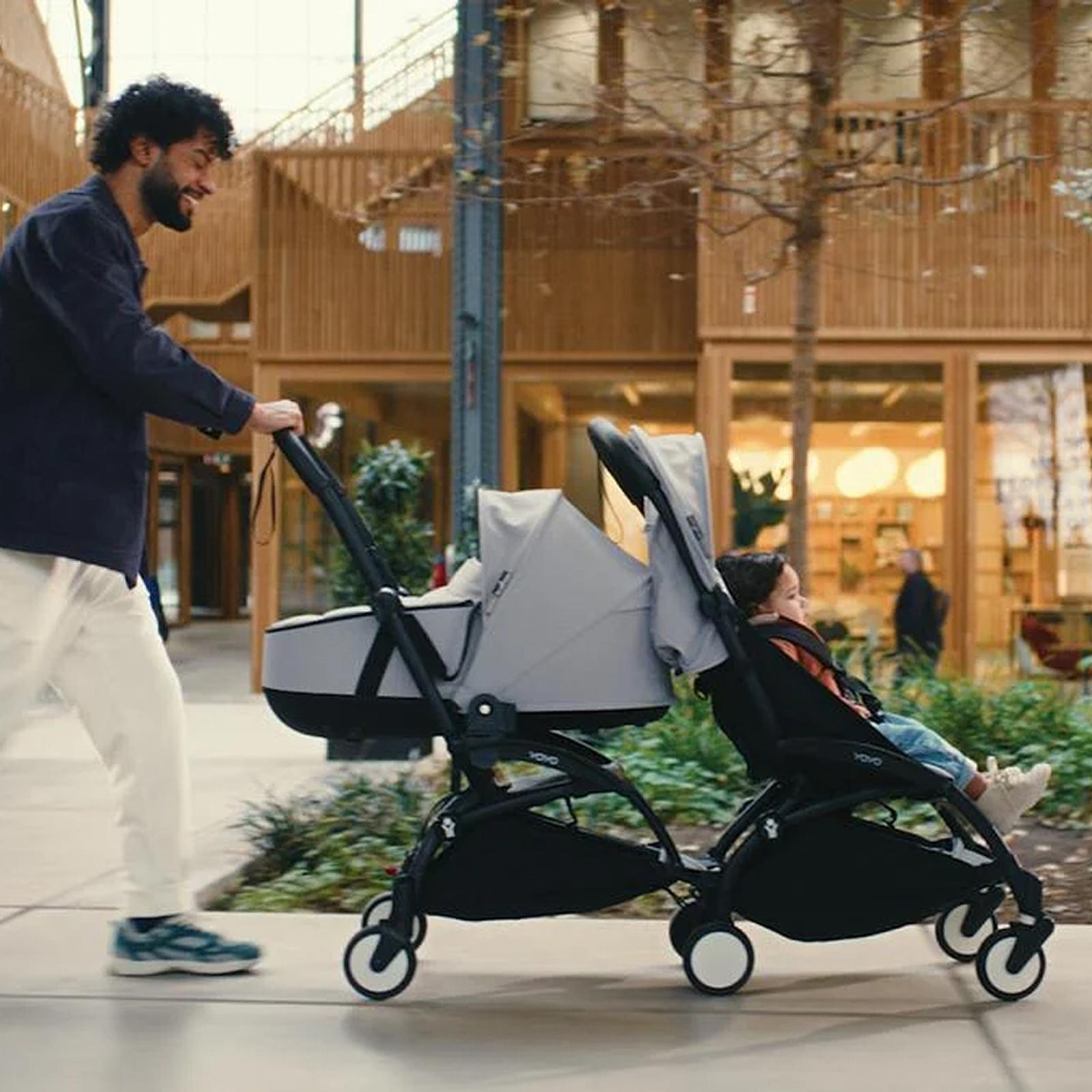 Uśmiechnięty mężczyzna pcha wózek STOKKE YOYO z dzieckiem w gondoli i dzieckiem w siedzisku.
