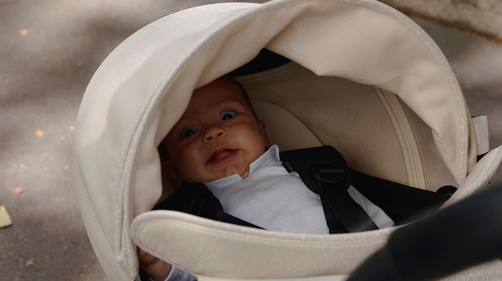 A happy baby looks up from a STOKKE YOYO stroller, sticking out their tongue.