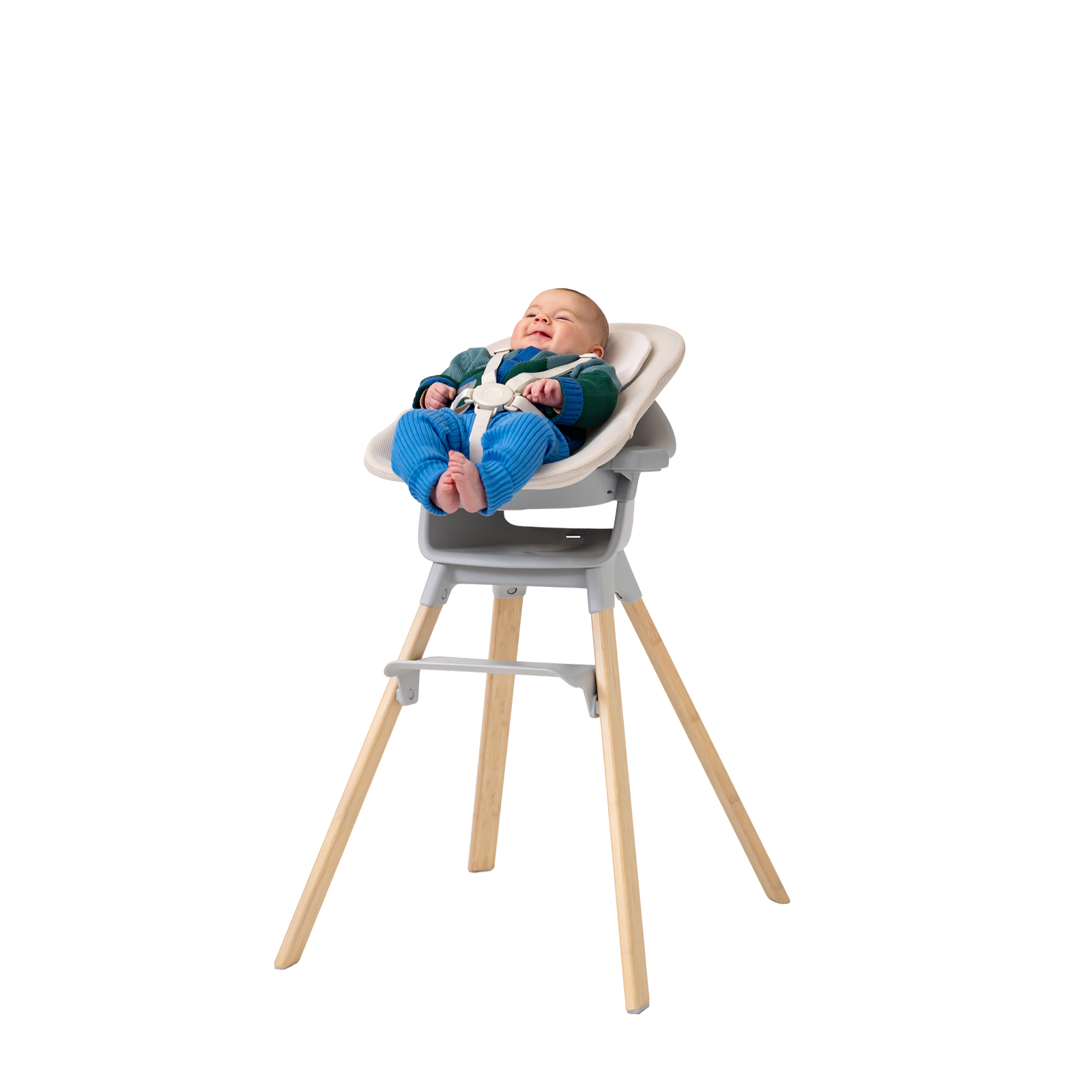 A smiling baby lies back in a grey high chair with a cream seat insert and wooden legs.