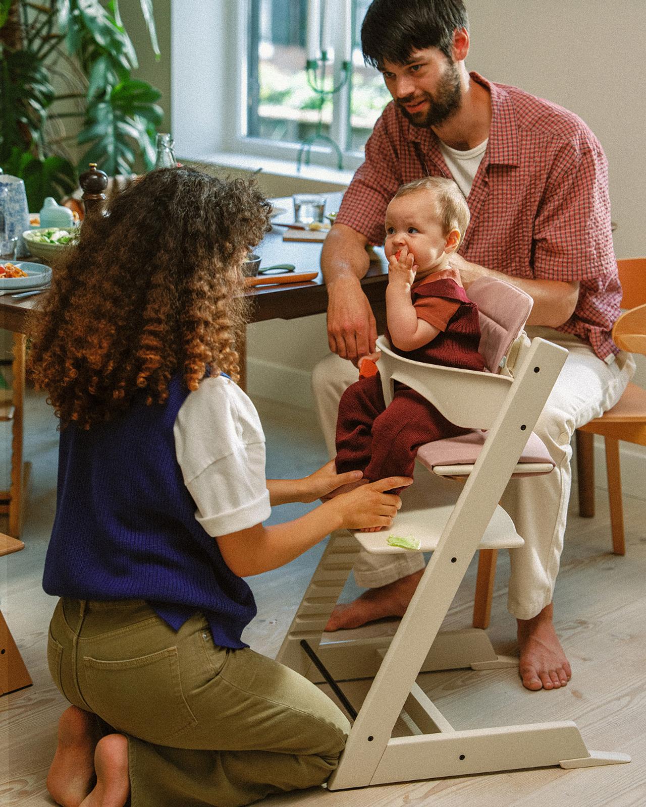 Familjen hjälper en bebis i en vit Tripp Trapp barnstol vid matbordet.