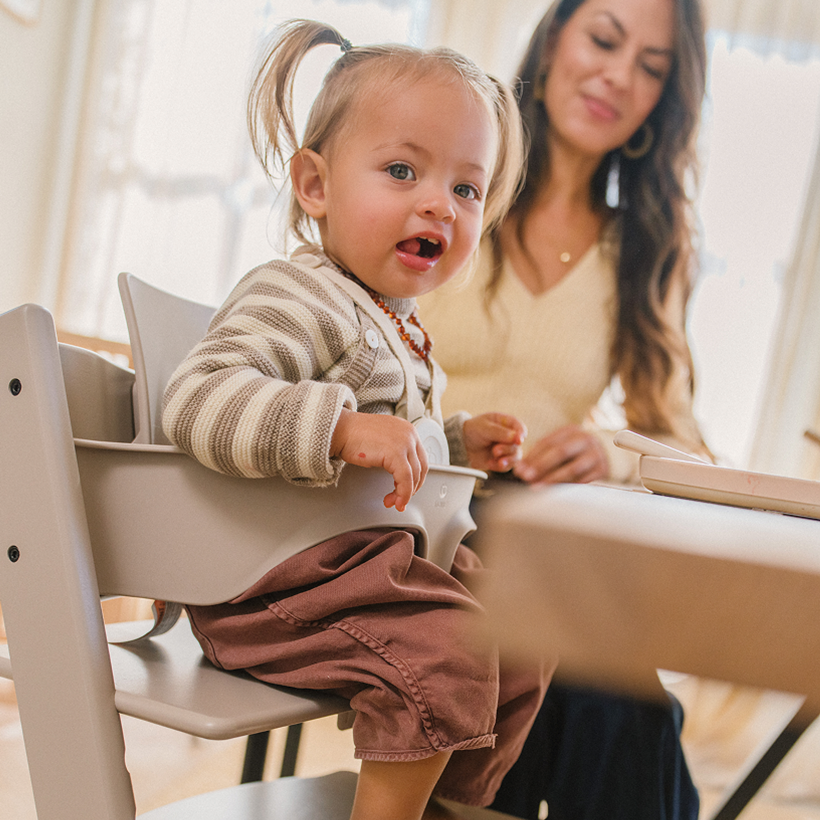 A cheerful toddler in a grey Tripp Trapp high chair looks at the camera.