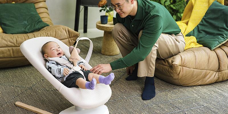 Father is playing with their child who is laying in the baby bouncer