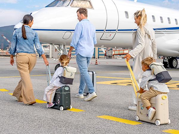 A family is boarding a plane with children who are riding on their JetKids luggage.​