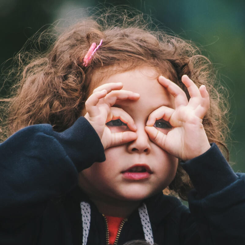 A young girl creating binoculars with her hands over her eyes to see nature more clearly. 