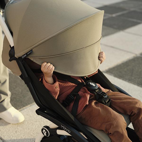 Jeune enfant assis dans une poussette Stokke YOYO avec canopy beige, prêt pour l’aventure.