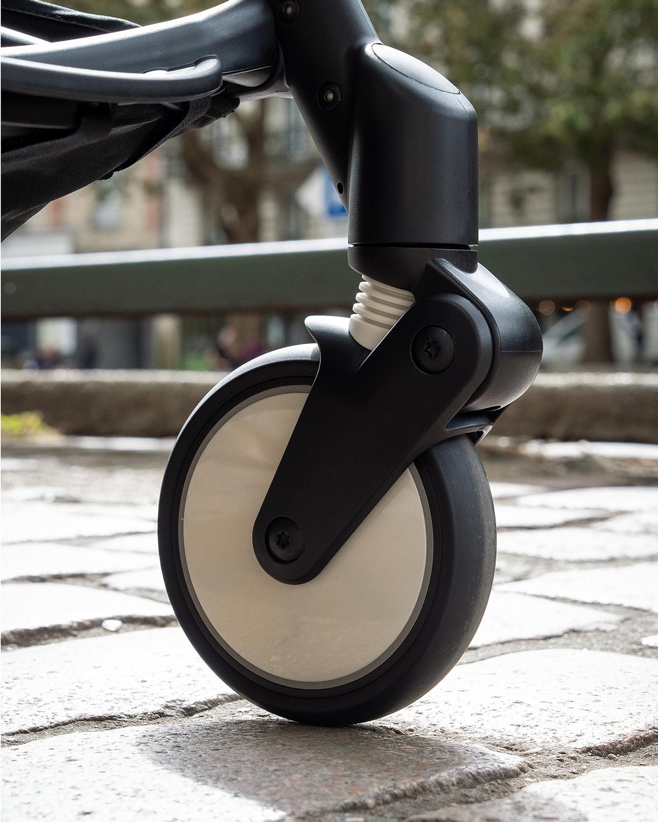 Close-up of a STOKKE YOYO stroller wheel and suspension on a paved street.