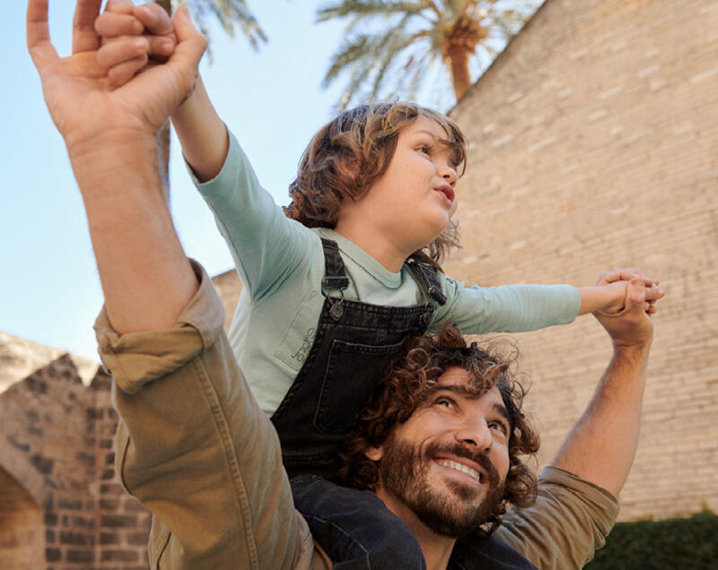 Child on father's shoulders pretending to fly.