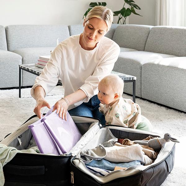 Mother packing the Flexibath, a collapsible baby bathtub, in her suitcase while her small baby watches.