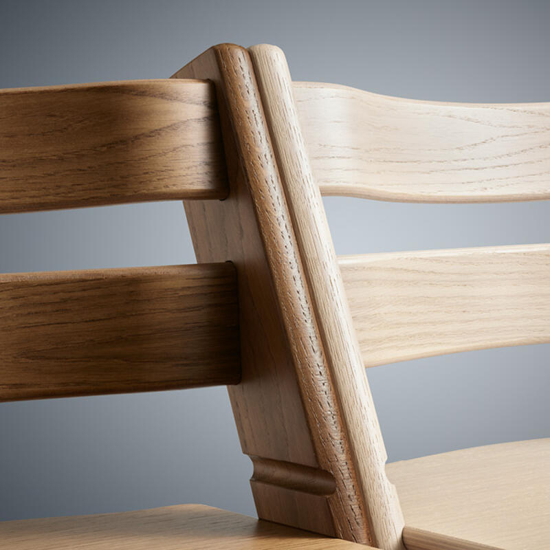 A closeup of Stokke Tripp Trapp chairs side by side displaying the wood grain in colors natural and oak brown.