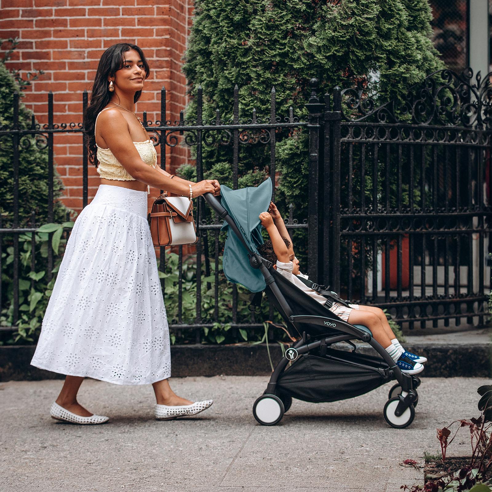 女性がSTOKKE YOYOベビーカーに乗った子供を歩道で押している。